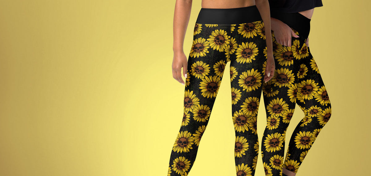 A pair of women's leggings with the new Sunflower Skulls pattern, illustrations of sunflowers with yellow petals and brown skull center, modeled on two women against a golden yellow background.